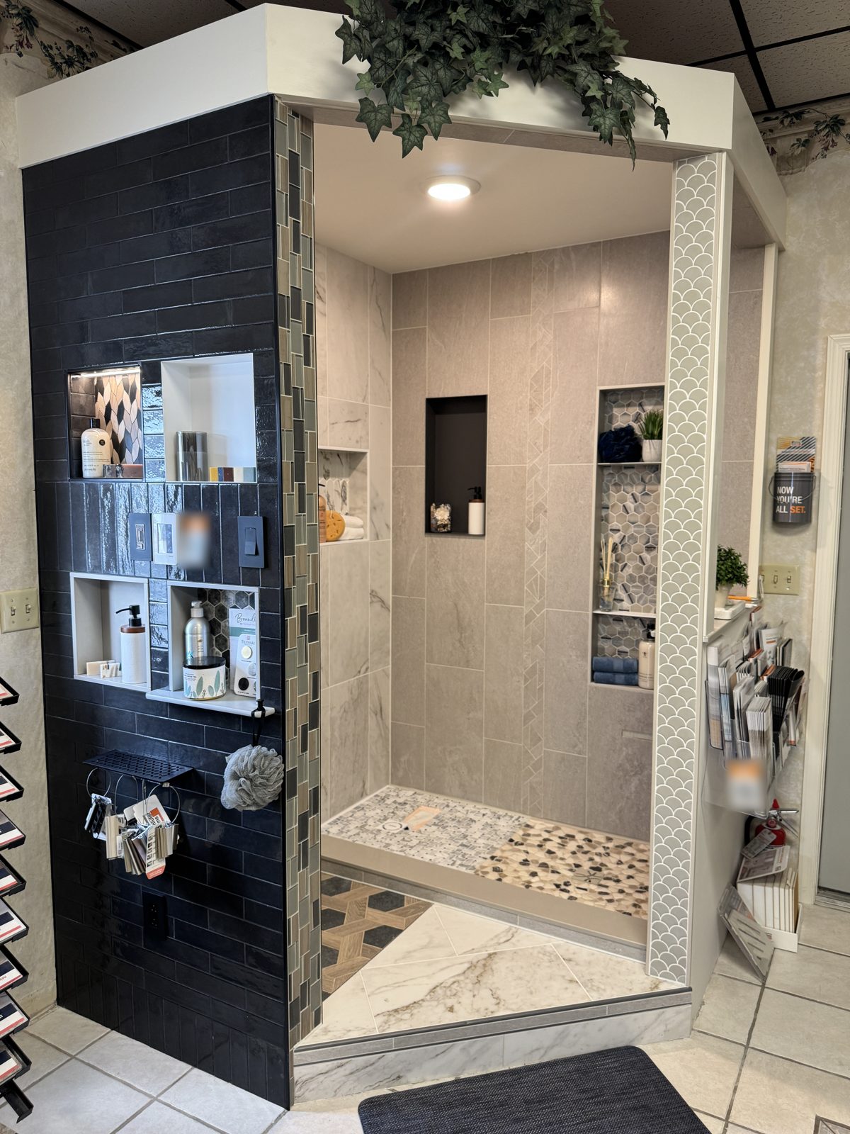 The display tile shower in the A & A showroom, with marble-look walls, recessed niches, a mosaic and pebble floor, and a navy subway tile exterior
