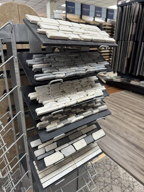 A rack of tumbled stone mosaic sheets in white, gray, and mixed tones